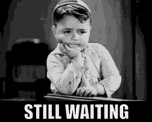 Animated gif in black and white of a young boy drumming his fingers with text reading "still waiting"